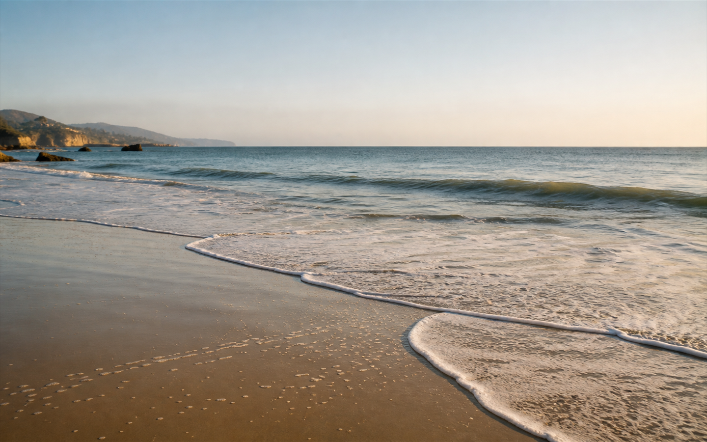 A calm early-morning shoreline with soft waves and clear light